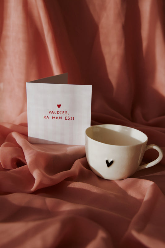 Porcelāna krūzīte ar melnu sirsniņu un apsveikuma kartīti